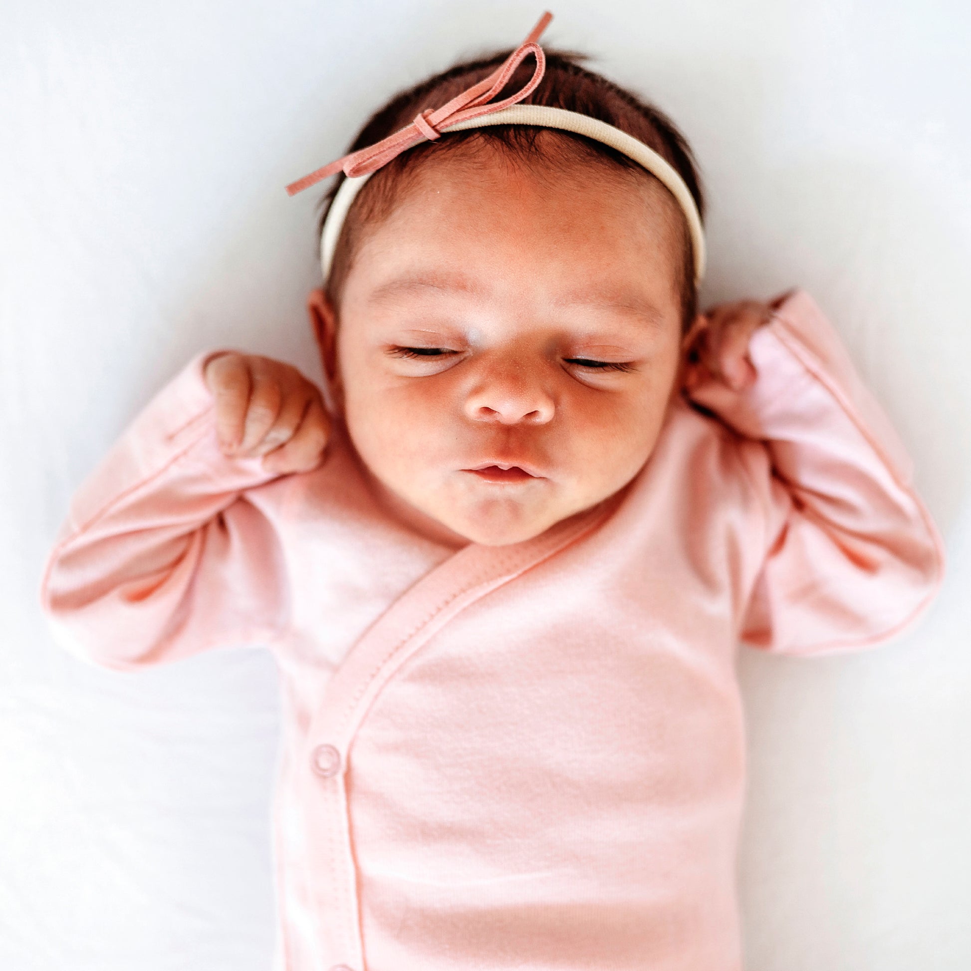 Newborn baby wearing a pink outfit and headband on a white background