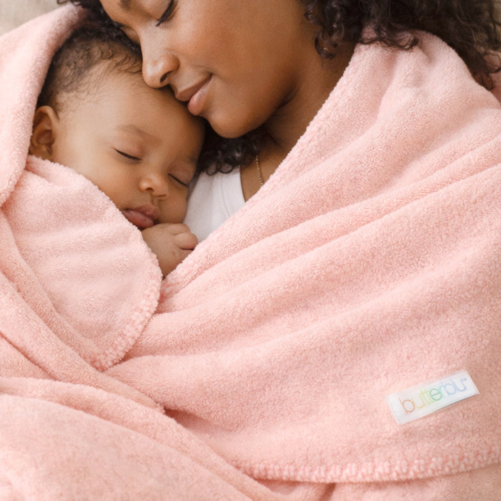Woman and child wrapped in a pink blanket with a visible brand label.