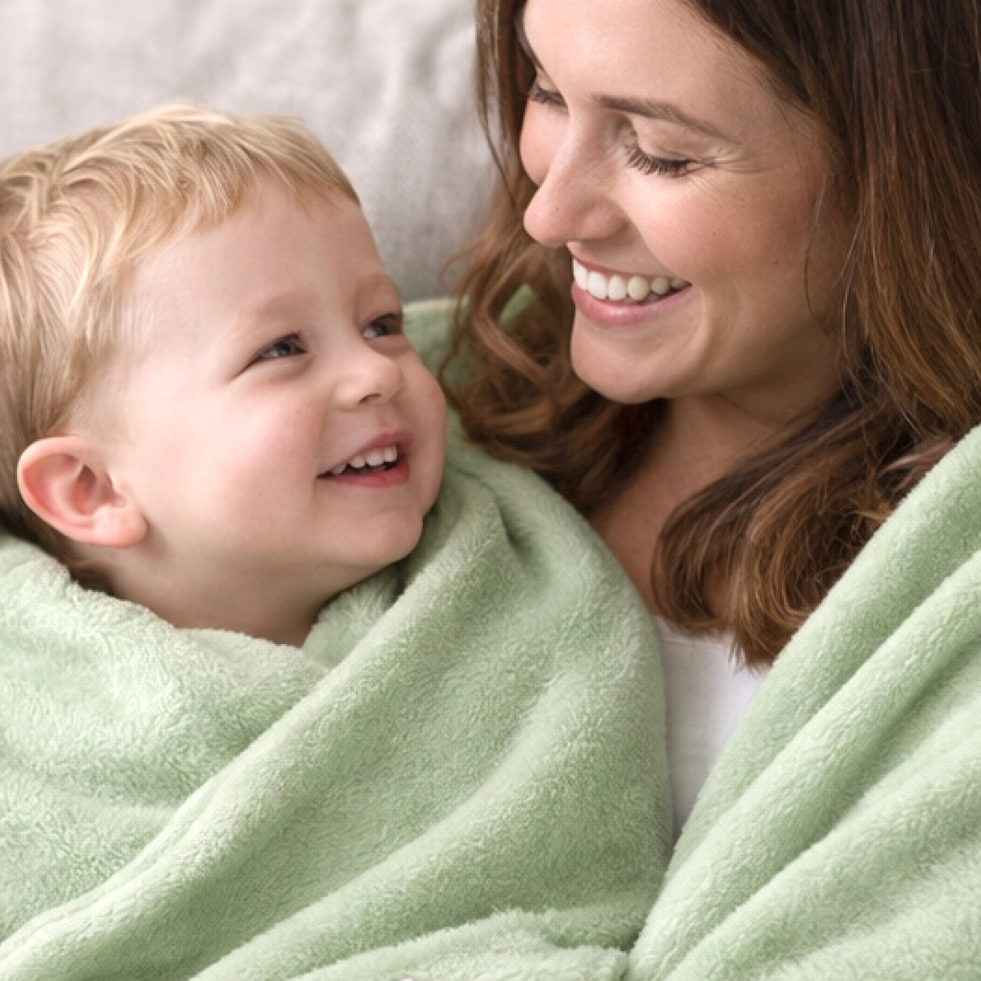 Woman and child wrapped in a green blanket, smiling at each other.