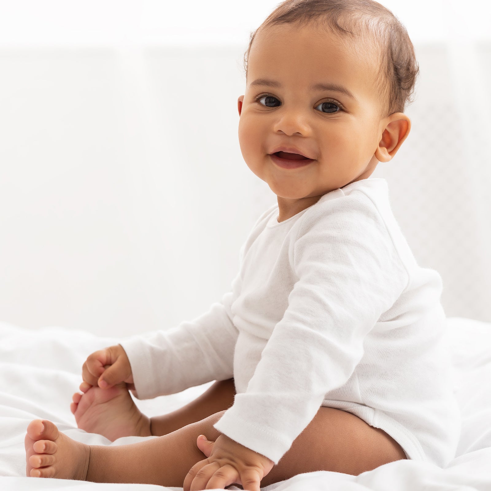 Baby in a white onesie sitting on a white surface