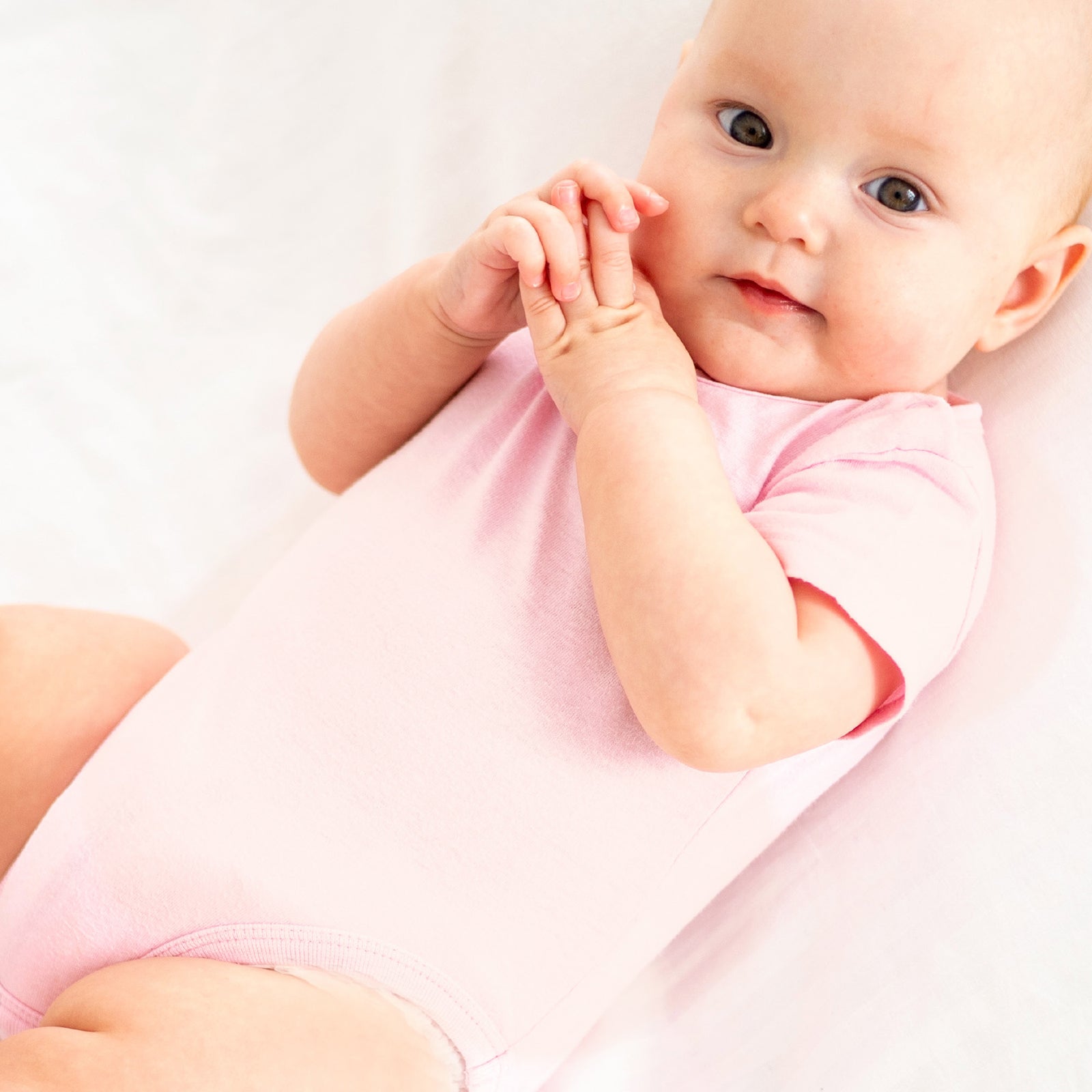Baby in a pink onesie sitting on a white background