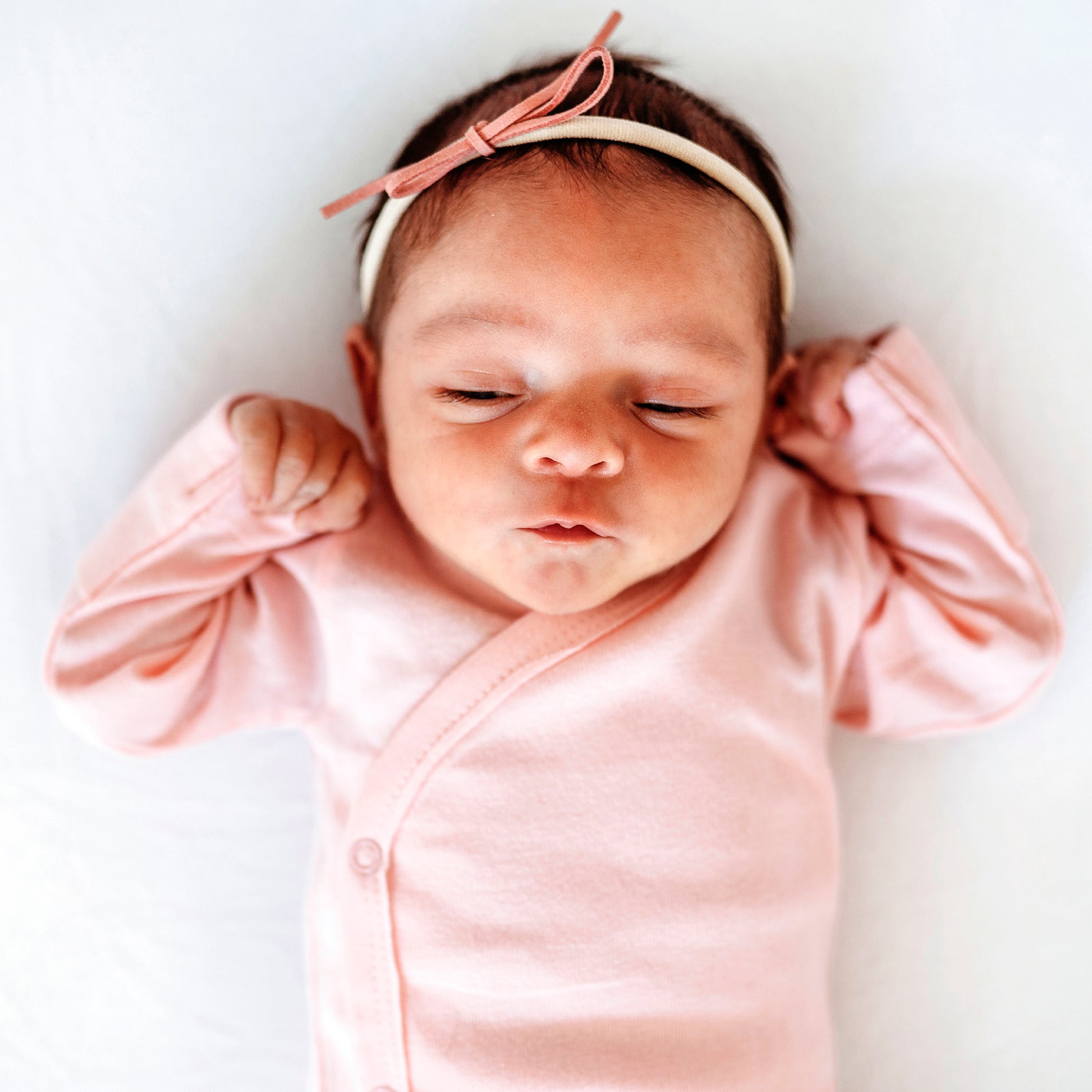 Newborn baby wearing a pink outfit and headband on a white background
