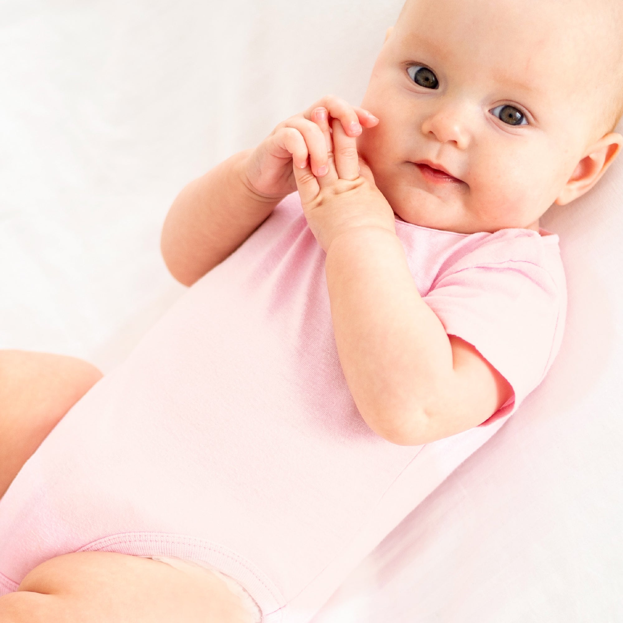 Baby in a pink onesie sitting on a white surface