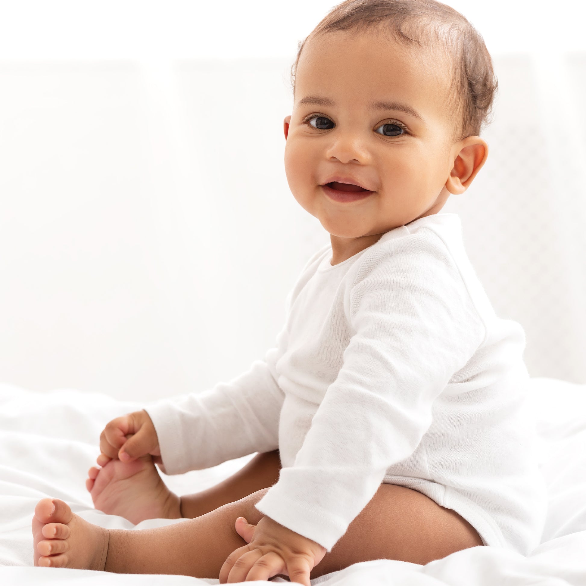 Baby in a white onesie sitting on a white surface
