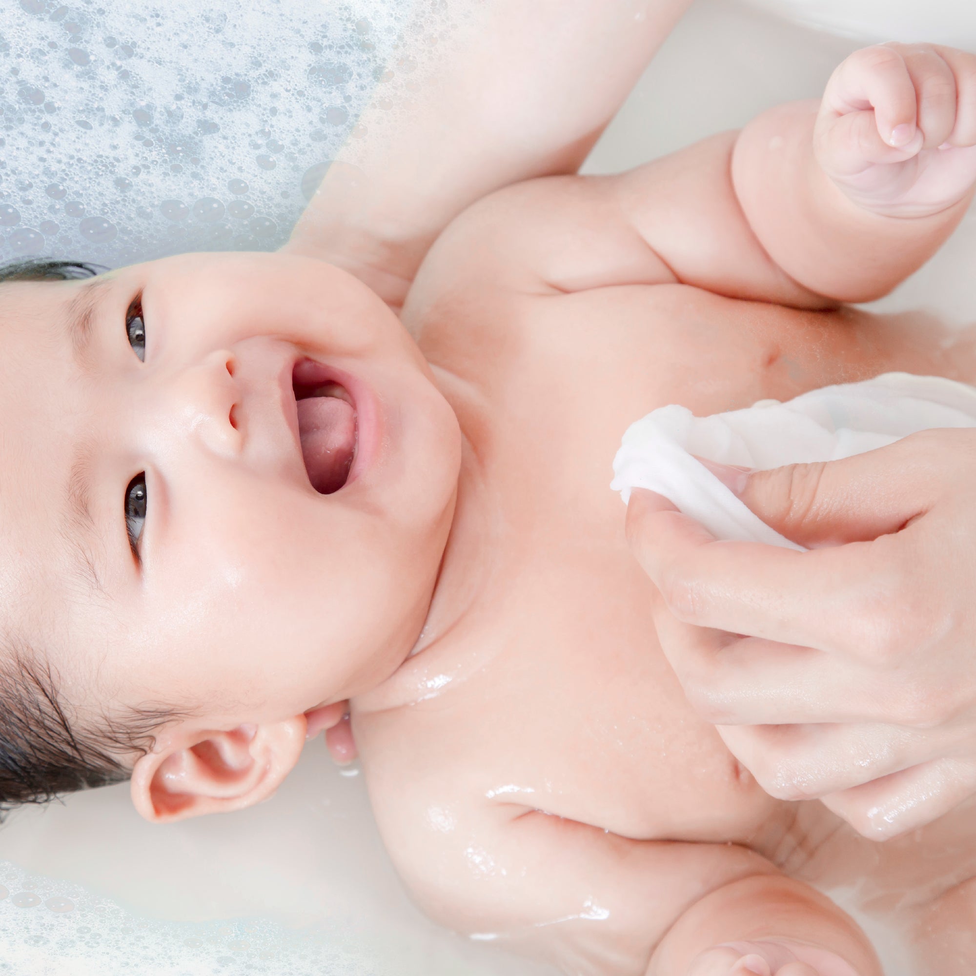 Baby being bathed with a white cloth in a bathtub