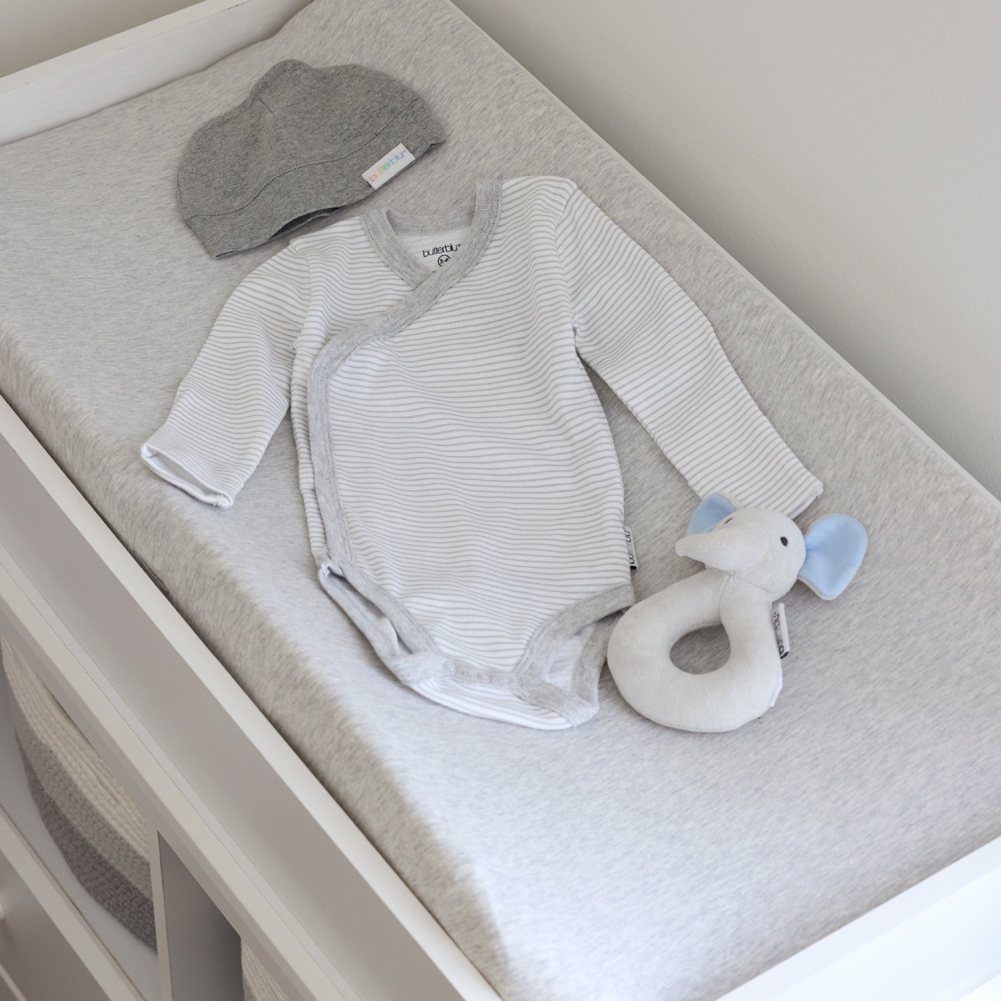 Baby outfit with striped onesie, gray hat, and white rattle on a changing table.
