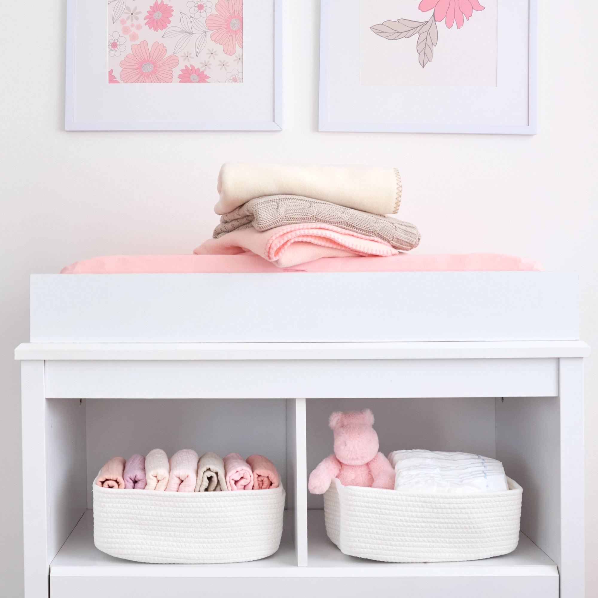 White changing table with folded baby clothes, a teddy bear, and baskets in a nursery setting.