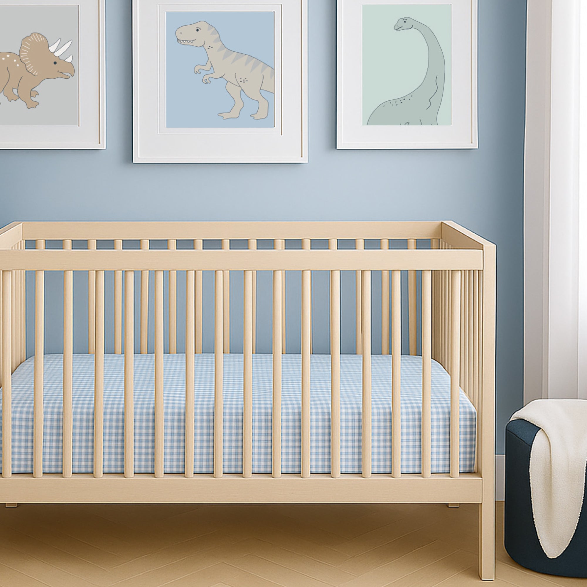 Wooden crib with blue checkered mattress in a room with dinosaur-themed wall art.