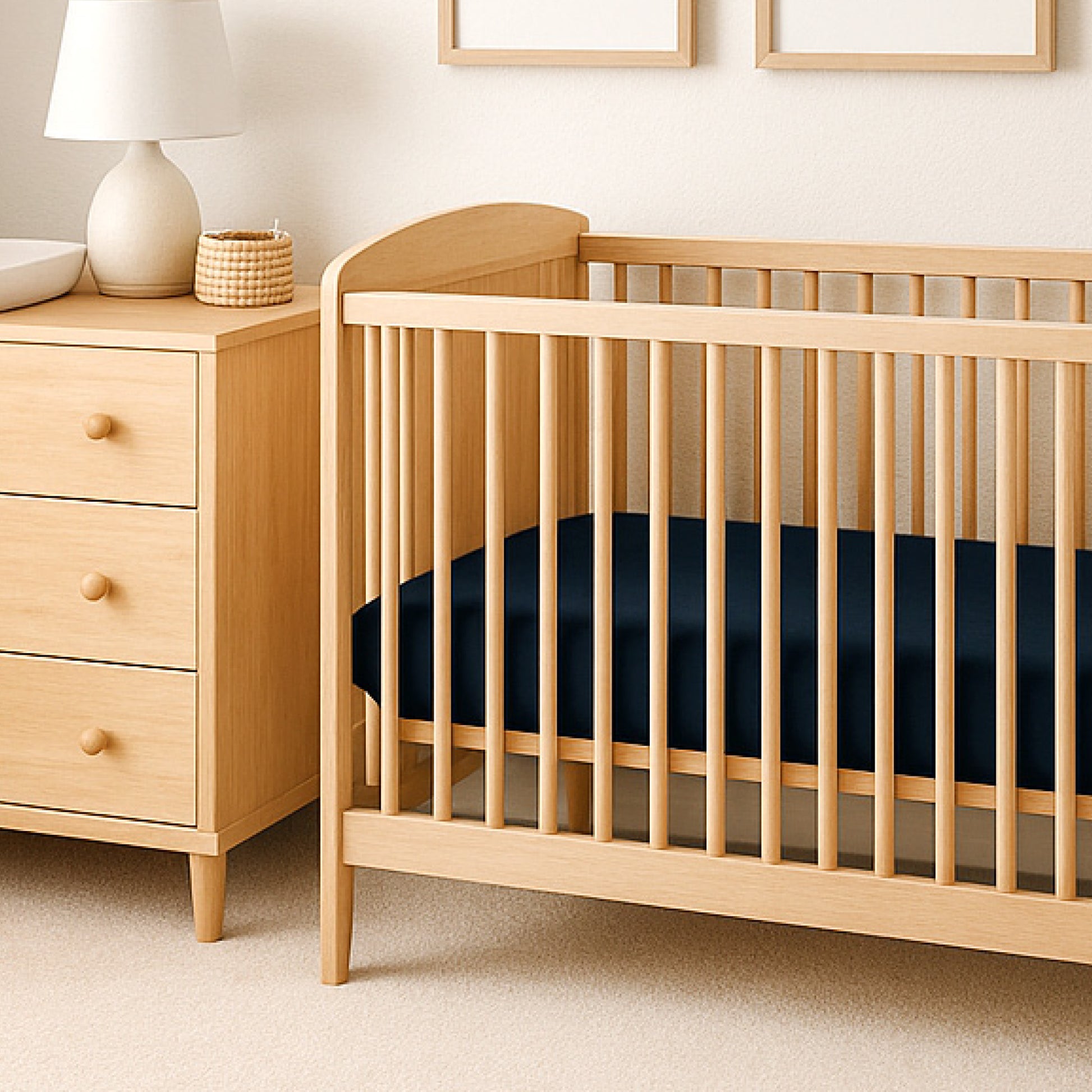 Wooden crib with black mattress next to a wooden dresser in a nursery.