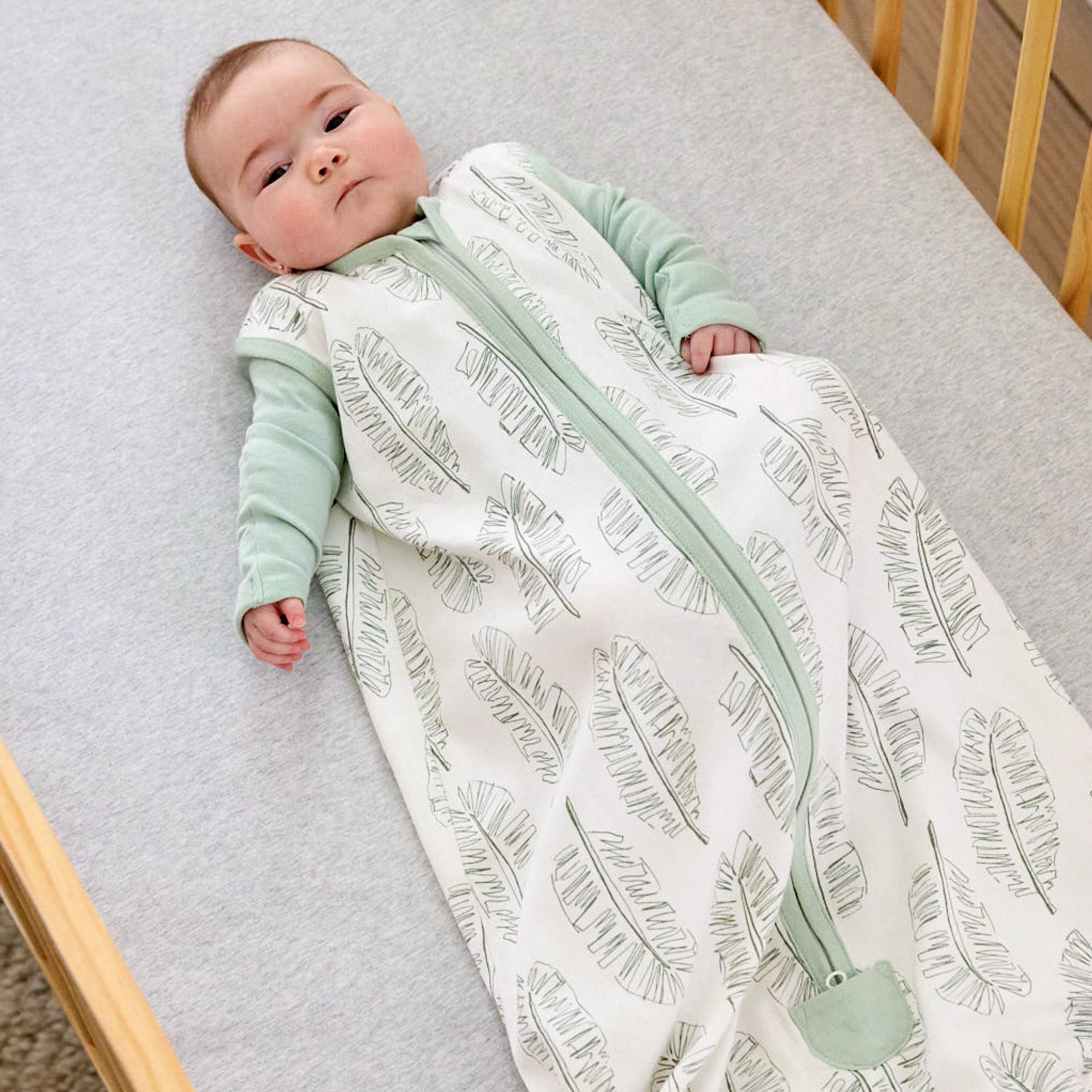Baby lying in a crib wearing a green and white patterned baby grow.