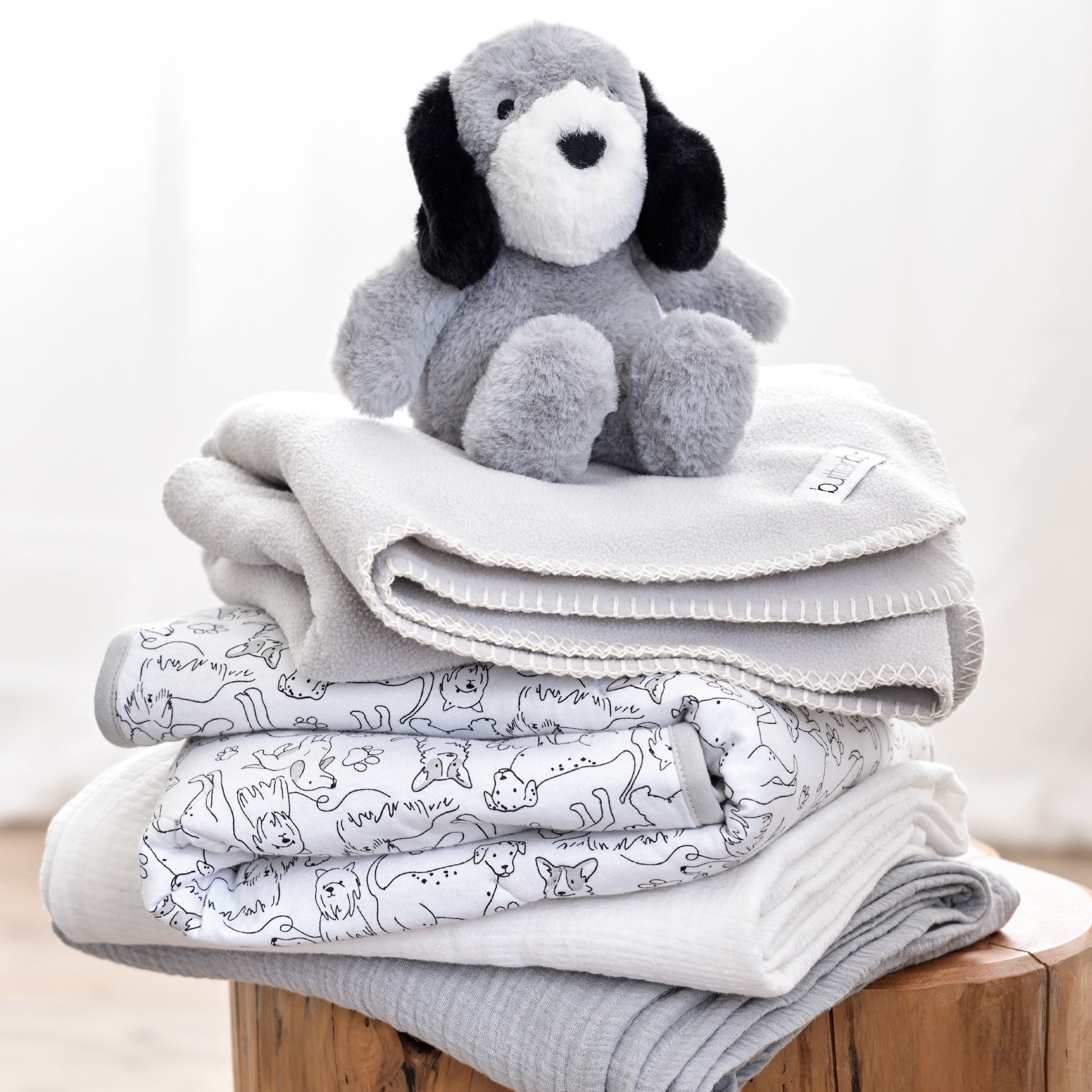 Stack of gray baby blankets with a soft toy on top against a white background