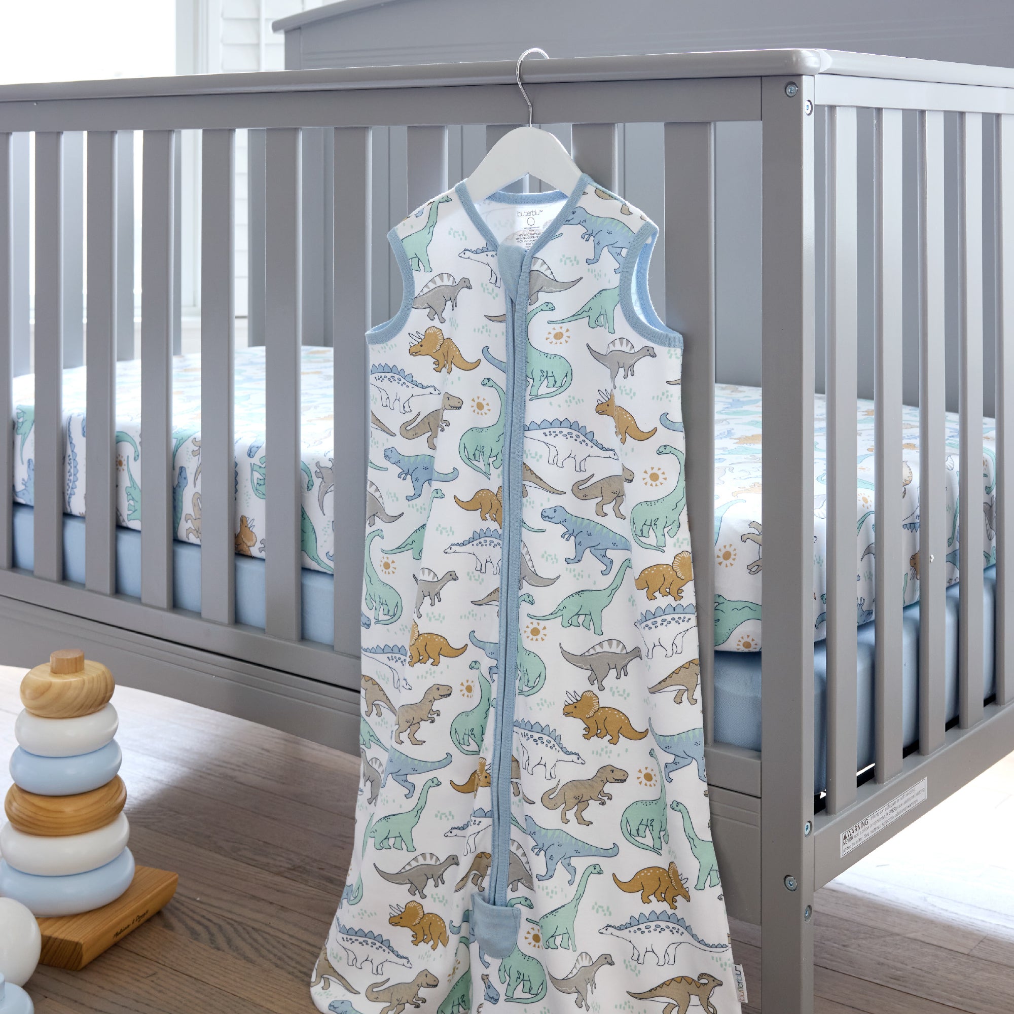Baby vest with dinosaur pattern hanging in front of a crib