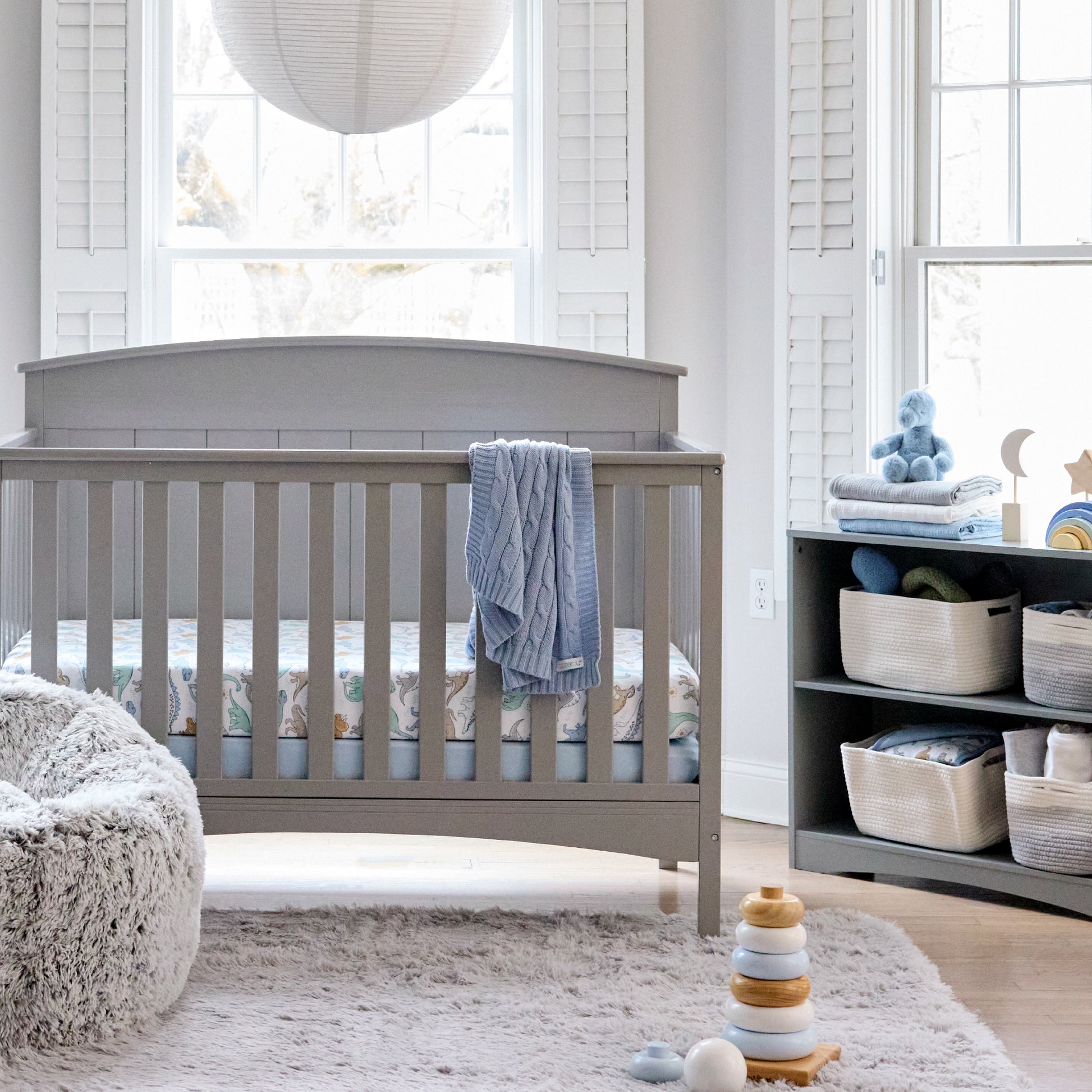 Nursery room with a gray crib, shelves, and toys in a bright room.