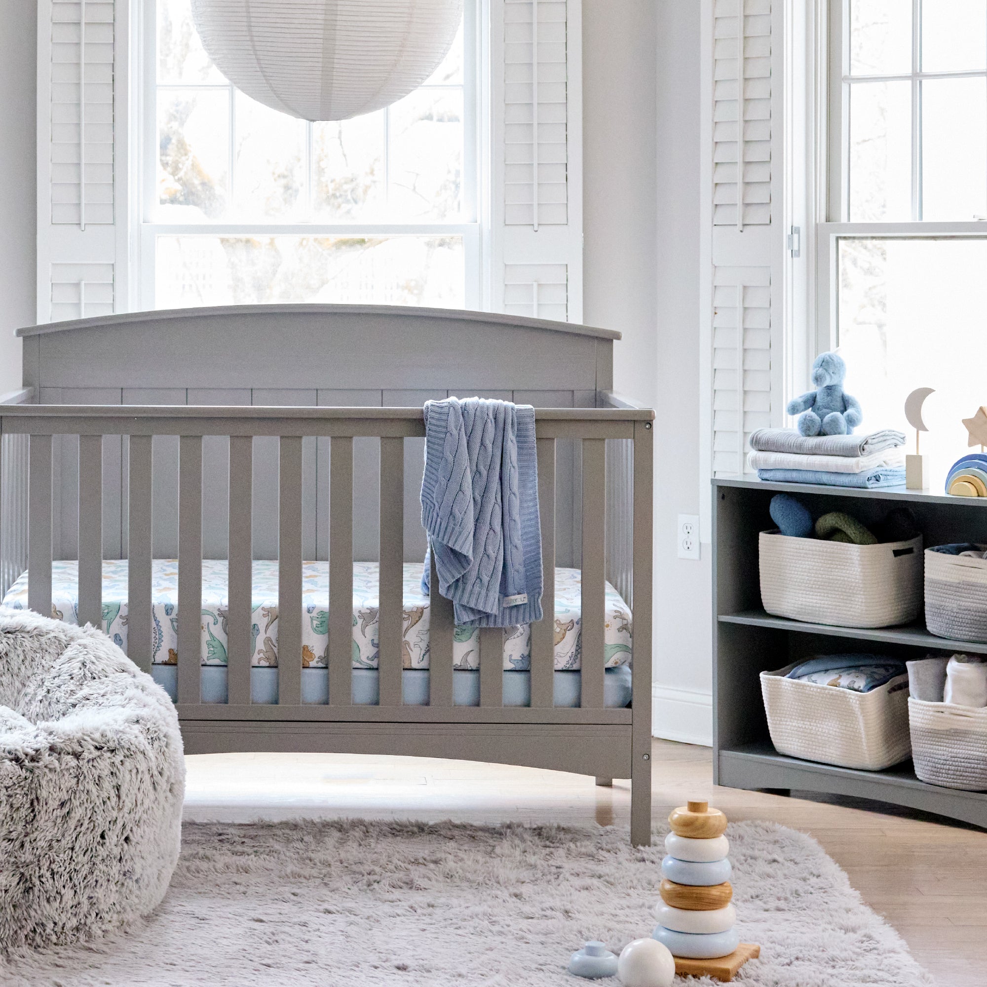 Nursery room with a gray crib, shelves, and toys in a bright room.