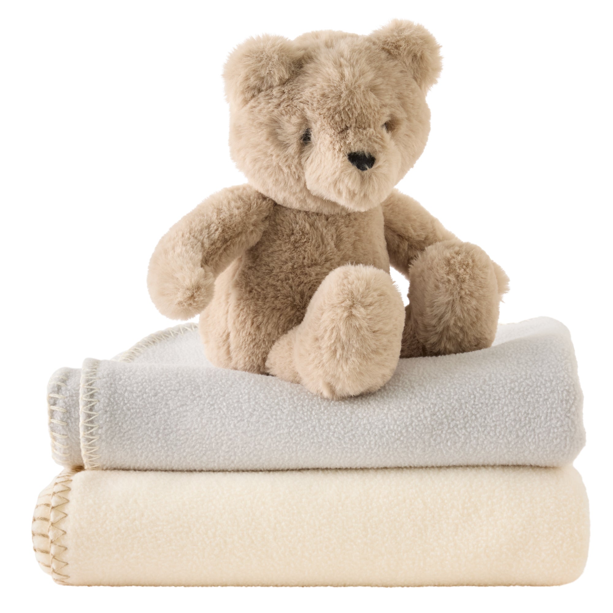 Plush teddy bear sitting on top of two folded towels, one gray and one beige, on a white background.