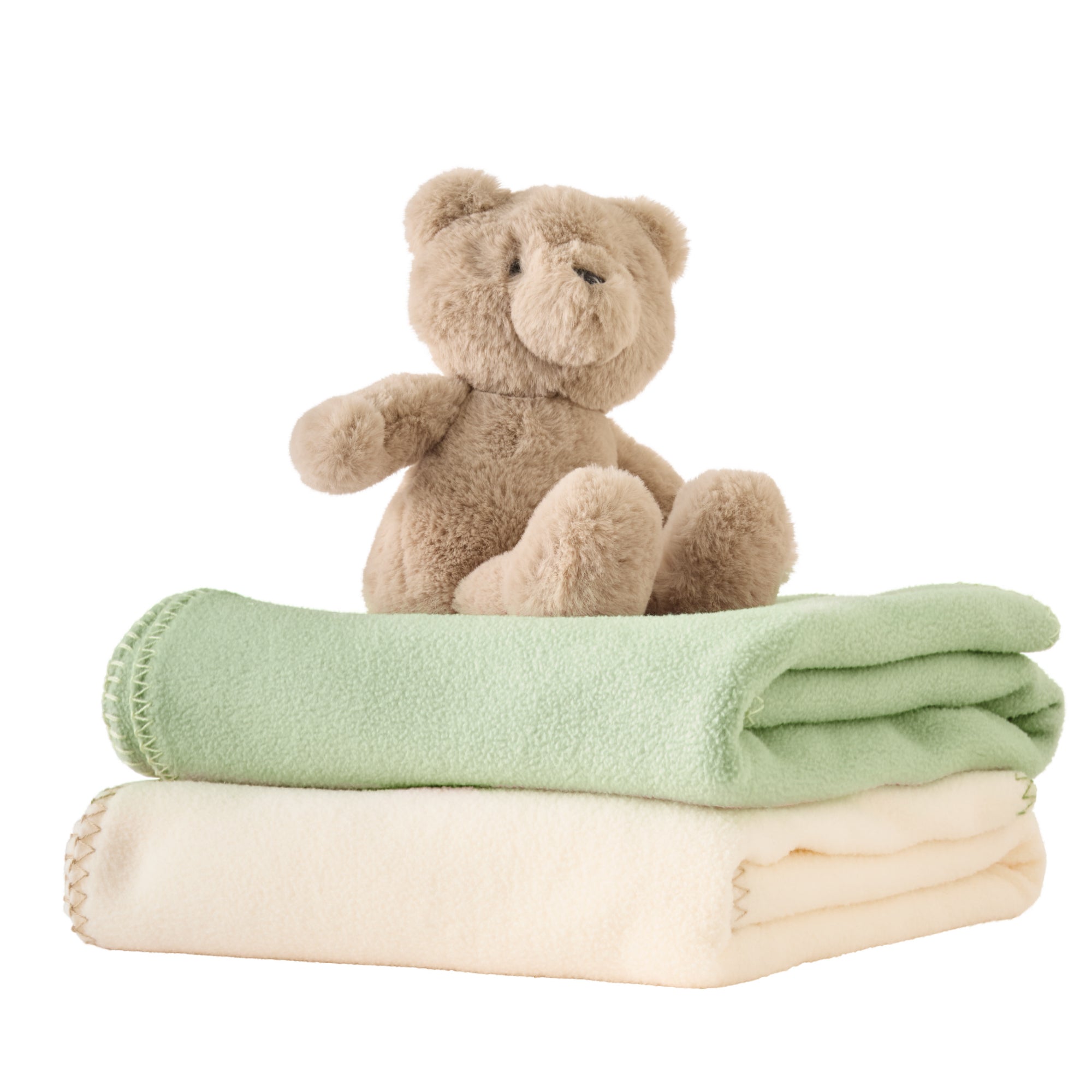 Teddy bear sitting on top of folded green and white blankets on a white background