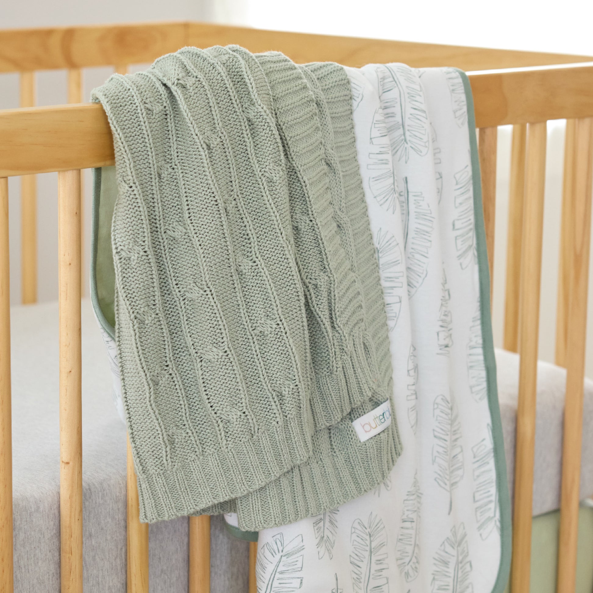 Green knitted blanket draped over a wooden crib with a white and green patterned blanket underneath.