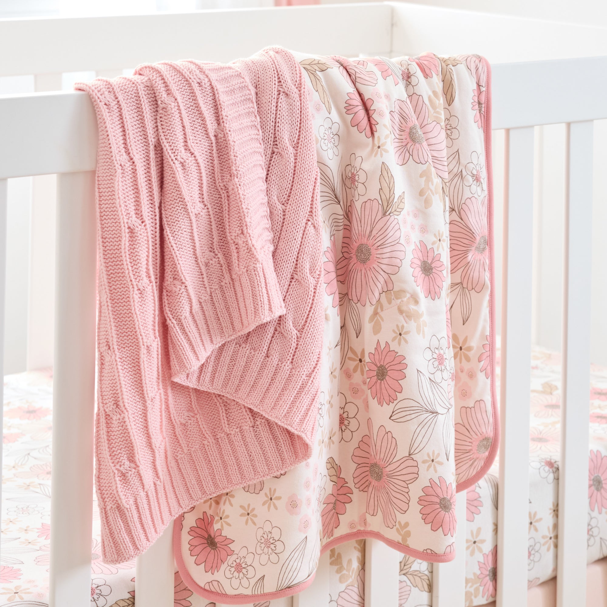 Pink knitted and floral-patterned blankets draped over a crib.