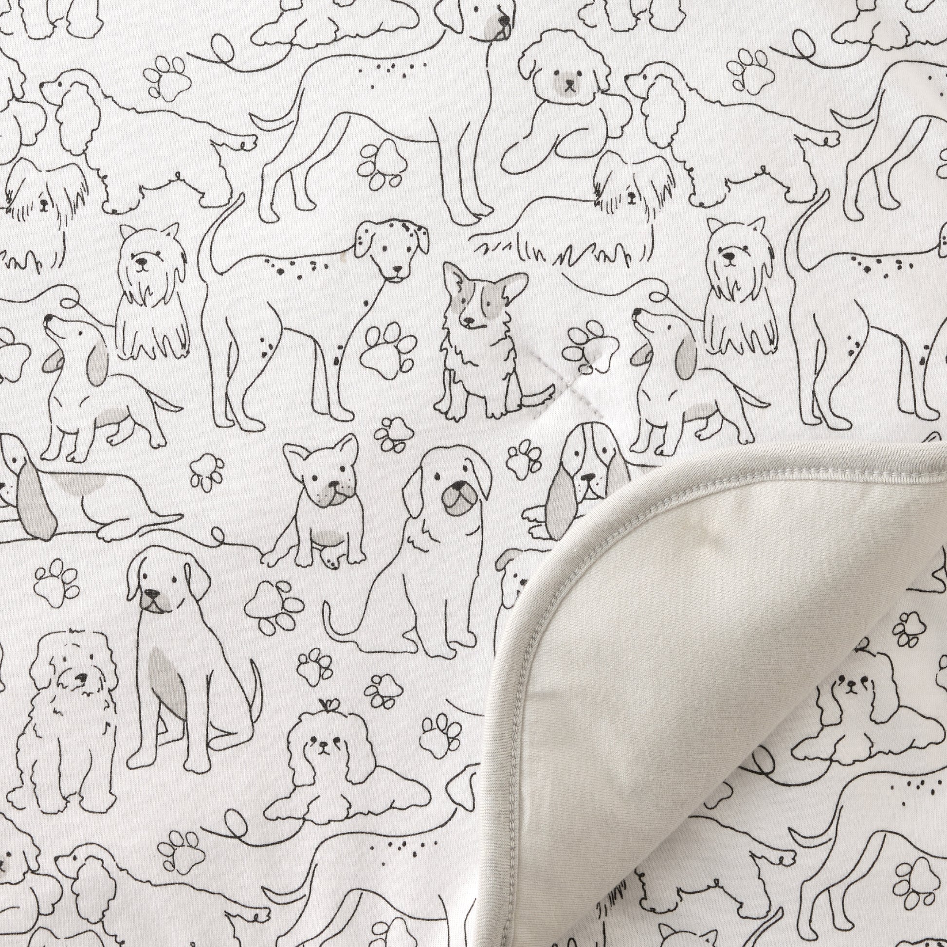 Pattern of black dogs and paw prints on a white background with a folded fabric edge.