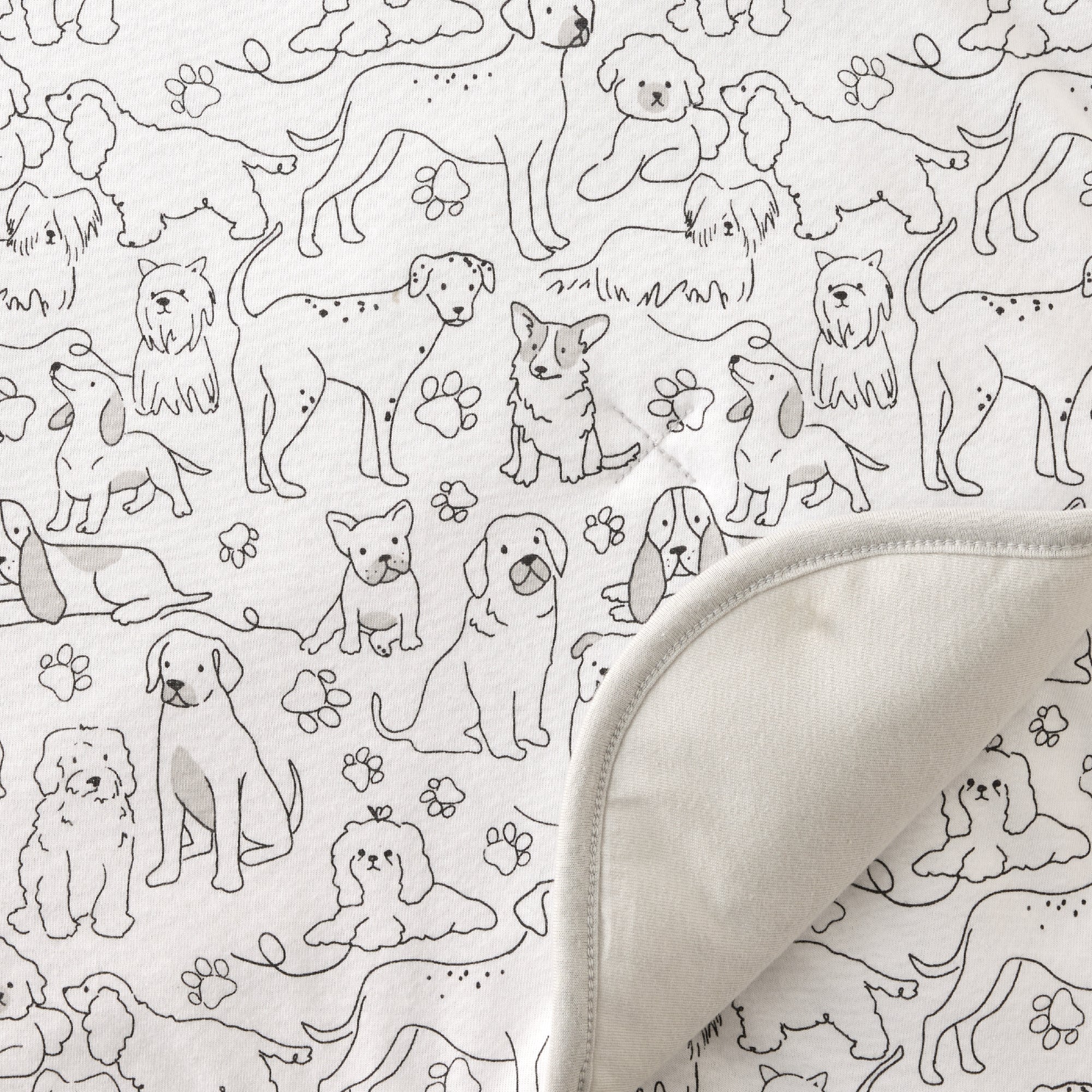 Pattern of black dogs and paw prints on a white background with a folded fabric edge.