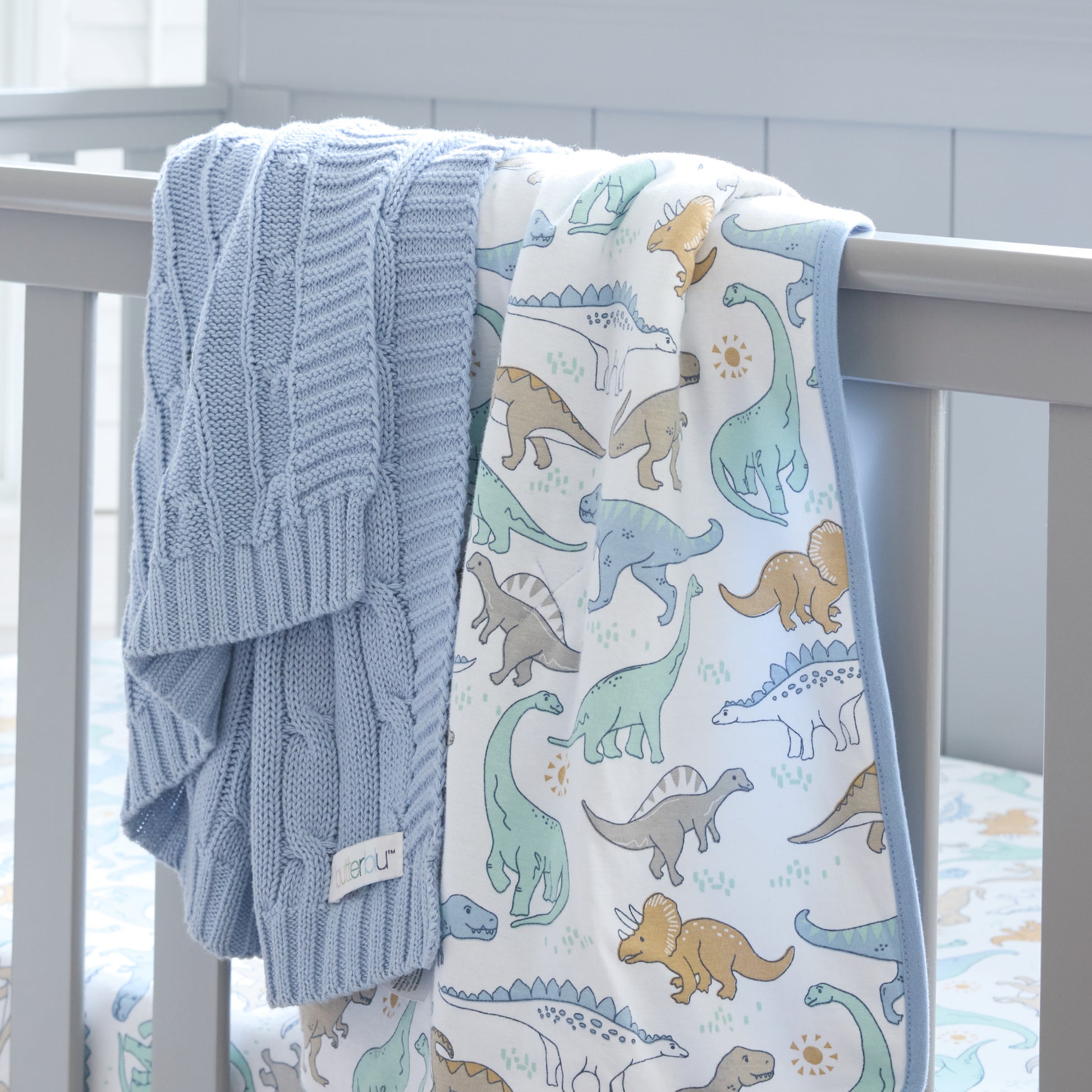 Blue knitted blanket and dinosaur-patterned blanket draped over a crib.