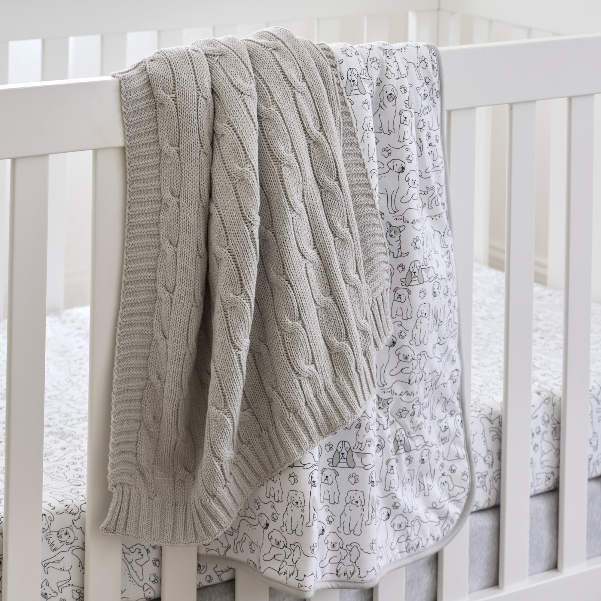 Gray cable knit blanket draped over a crib with a patterned gray sheet underneath.