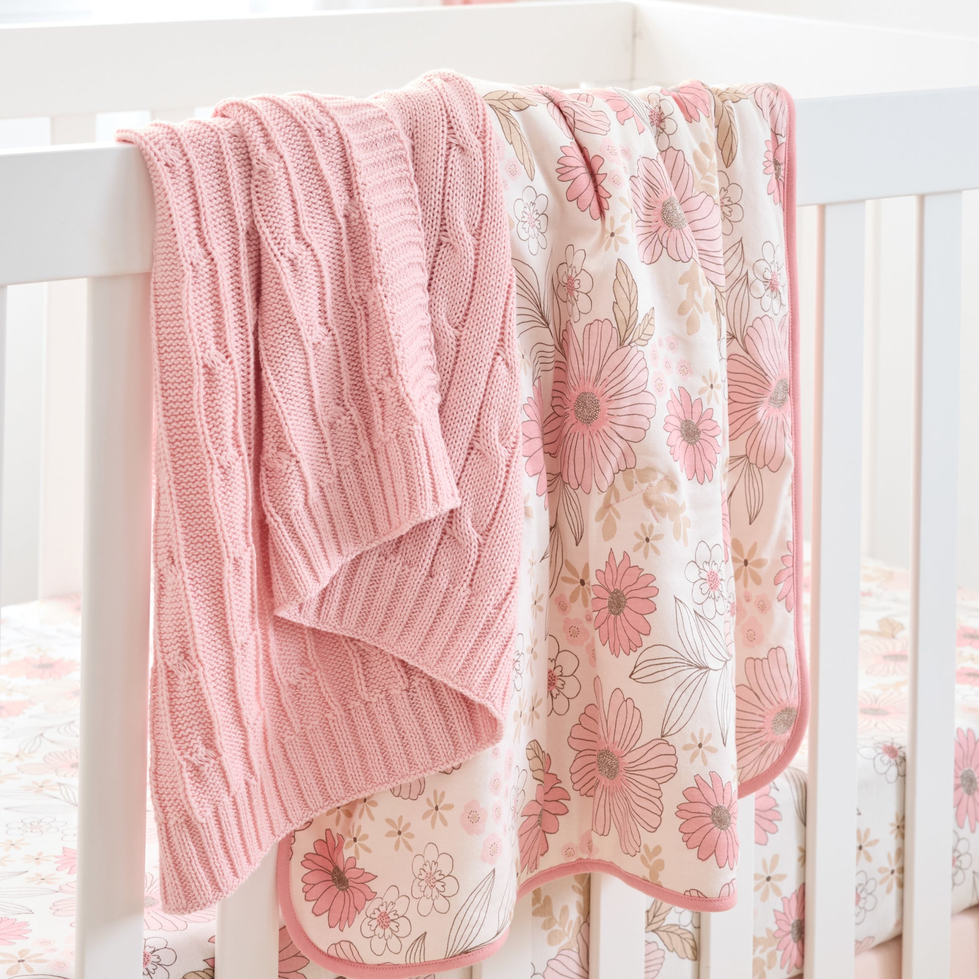 Pink knitted blanket and floral-patterned quilt draped over a crib.