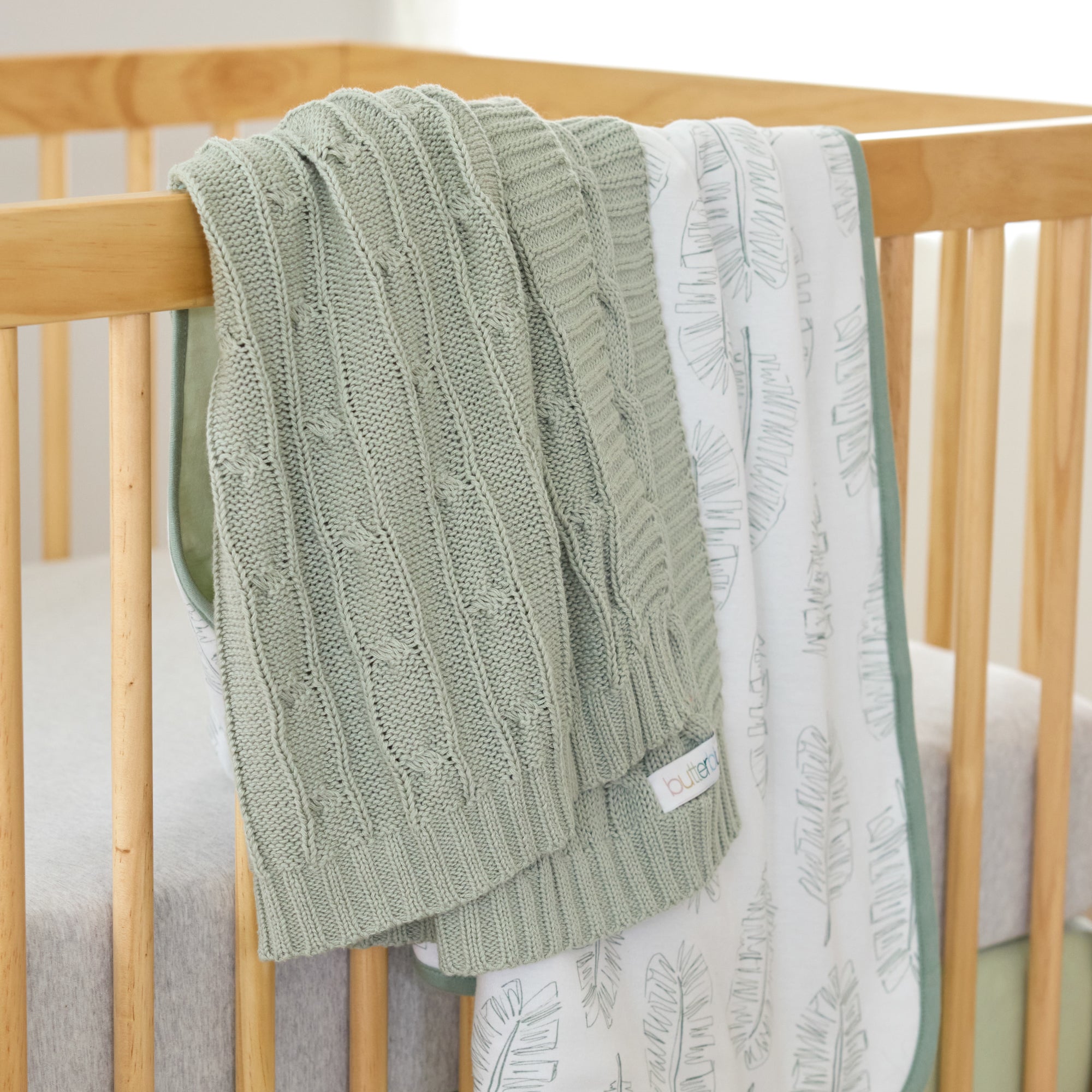 Green knitted blanket draped over a wooden crib with a white textured blanket underneath.