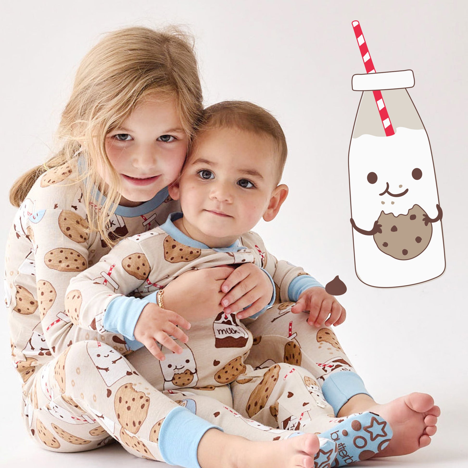 Two children in cookie-themed pajamas with a cartoon milk bottle and cookie graphic on a white background.