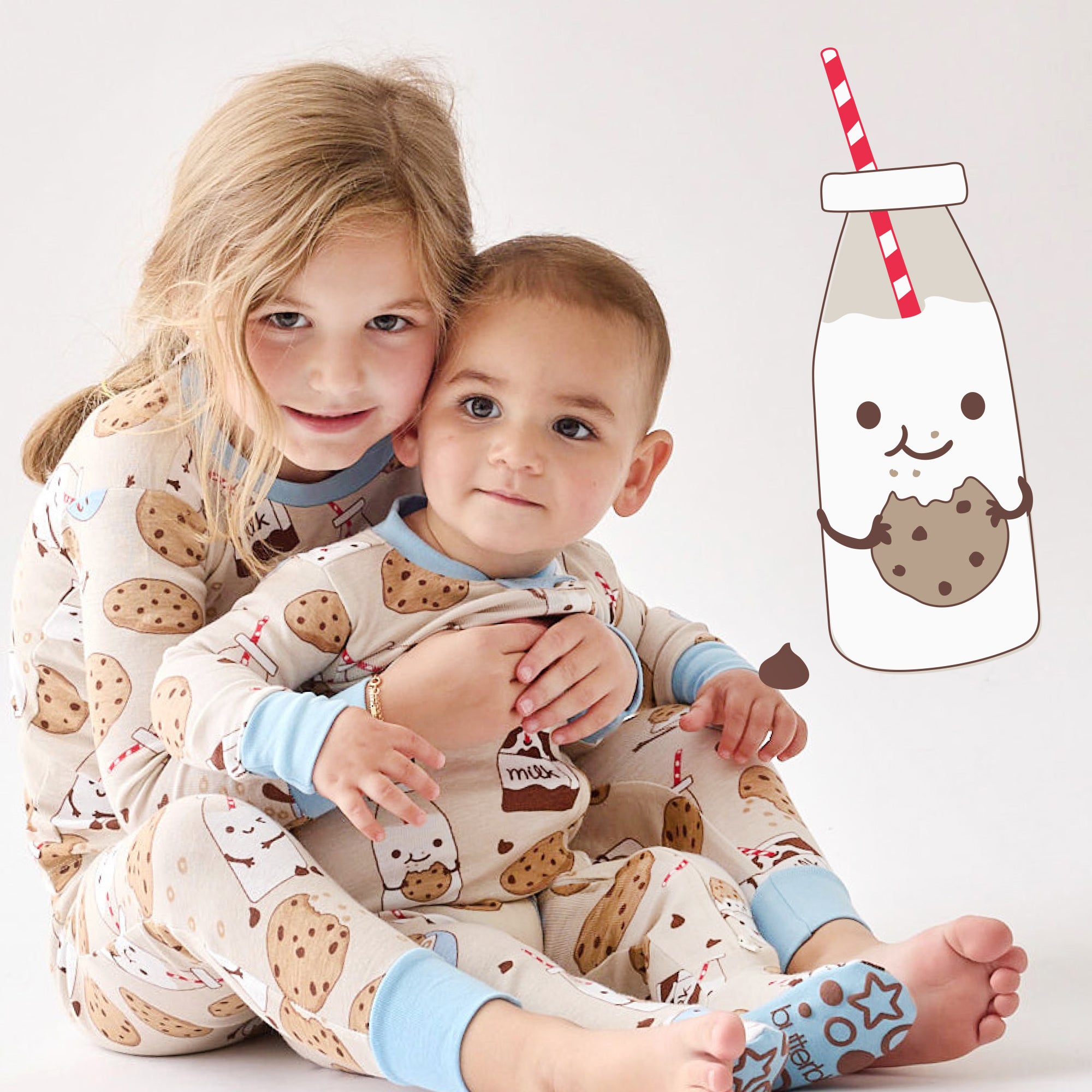 Two children in cookie-themed pajamas with a cartoon milk bottle and cookie graphic on a white background.