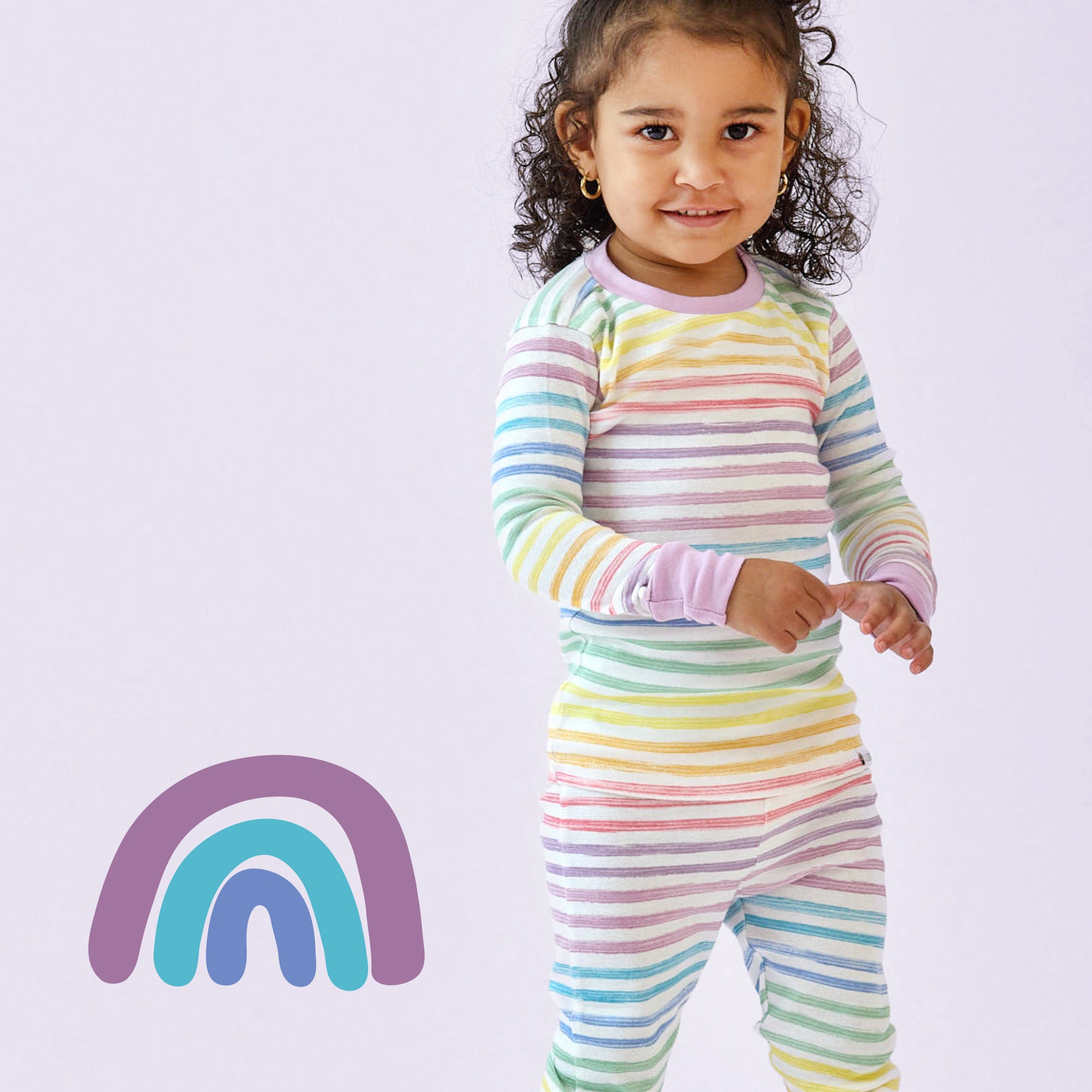 Child wearing a rainbow striped onesie with a rainbow graphic on a light purple background