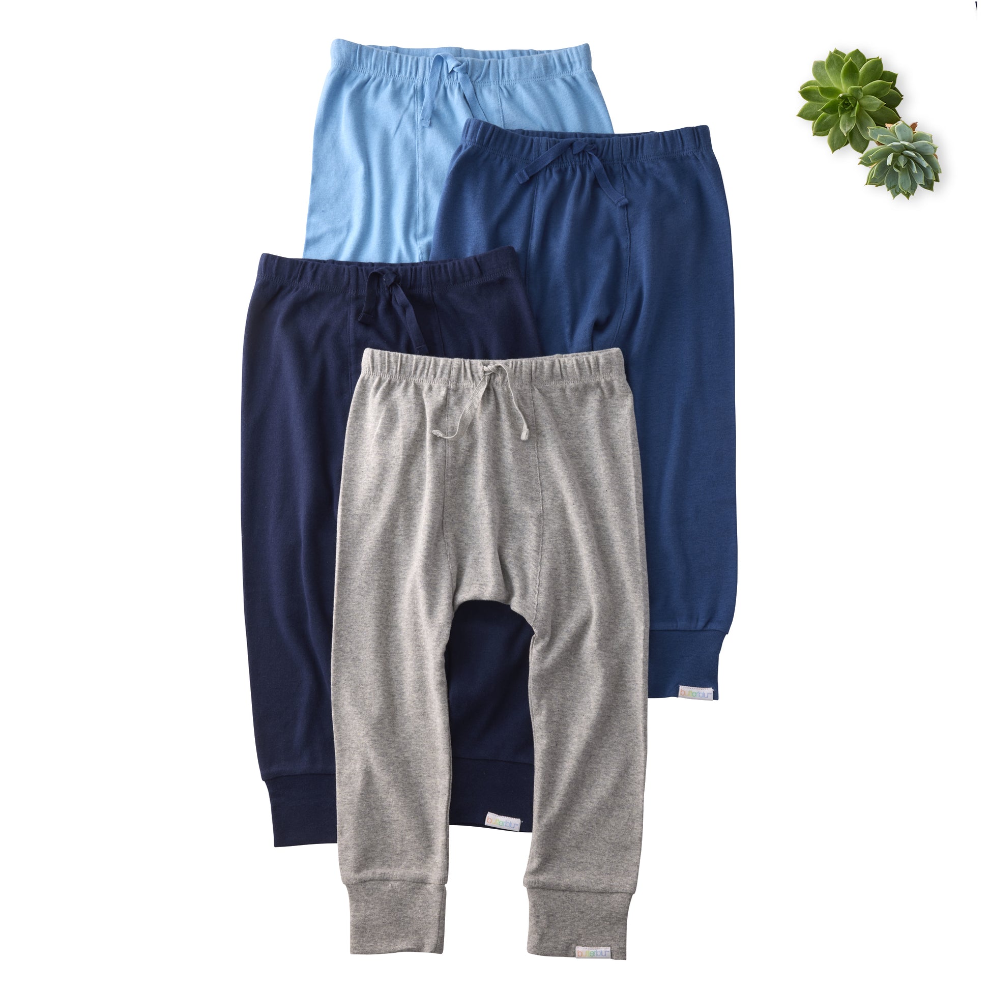 Three pairs of children's pants in blue, gray, and navy on a white background with a succulent plant.
