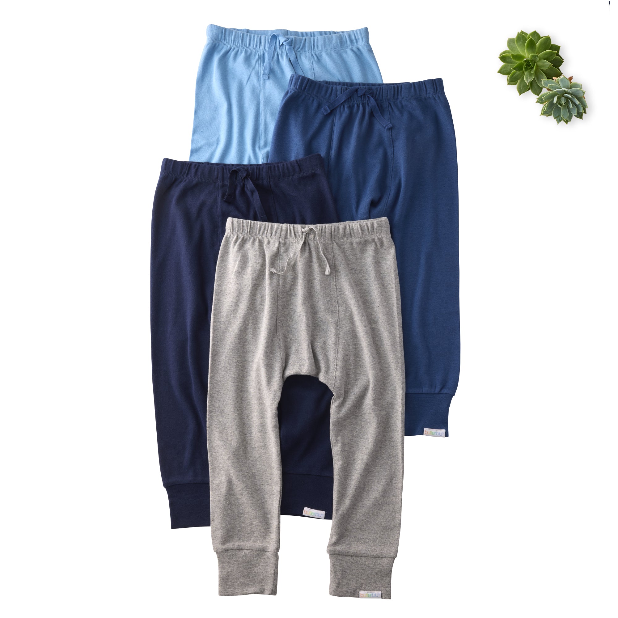 Three pairs of children's pants in blue, gray, and navy on a white background with a succulent plant.