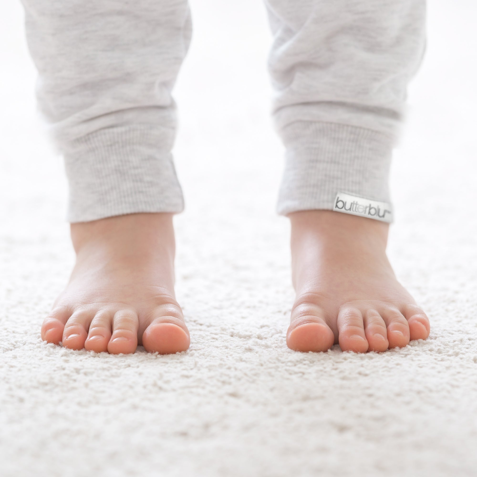 Baby's feet wearing gray pants with 'butterblu' brand logo on a white background