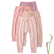 Three pairs of pink baby pants stacked on a white background with a flower.