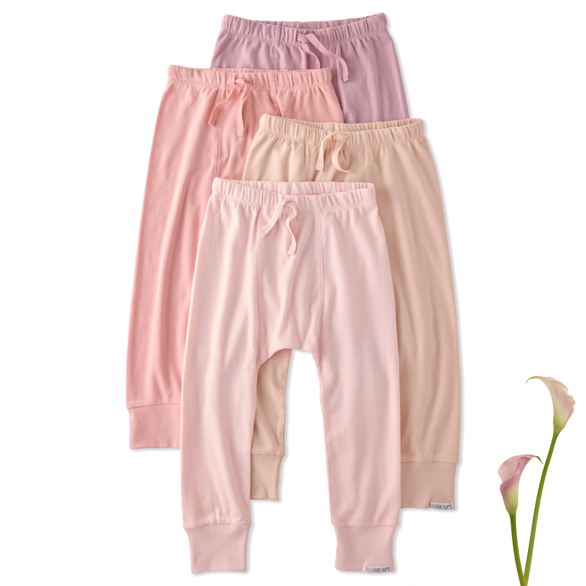 Three pairs of pink baby pants stacked on a white background with a flower.