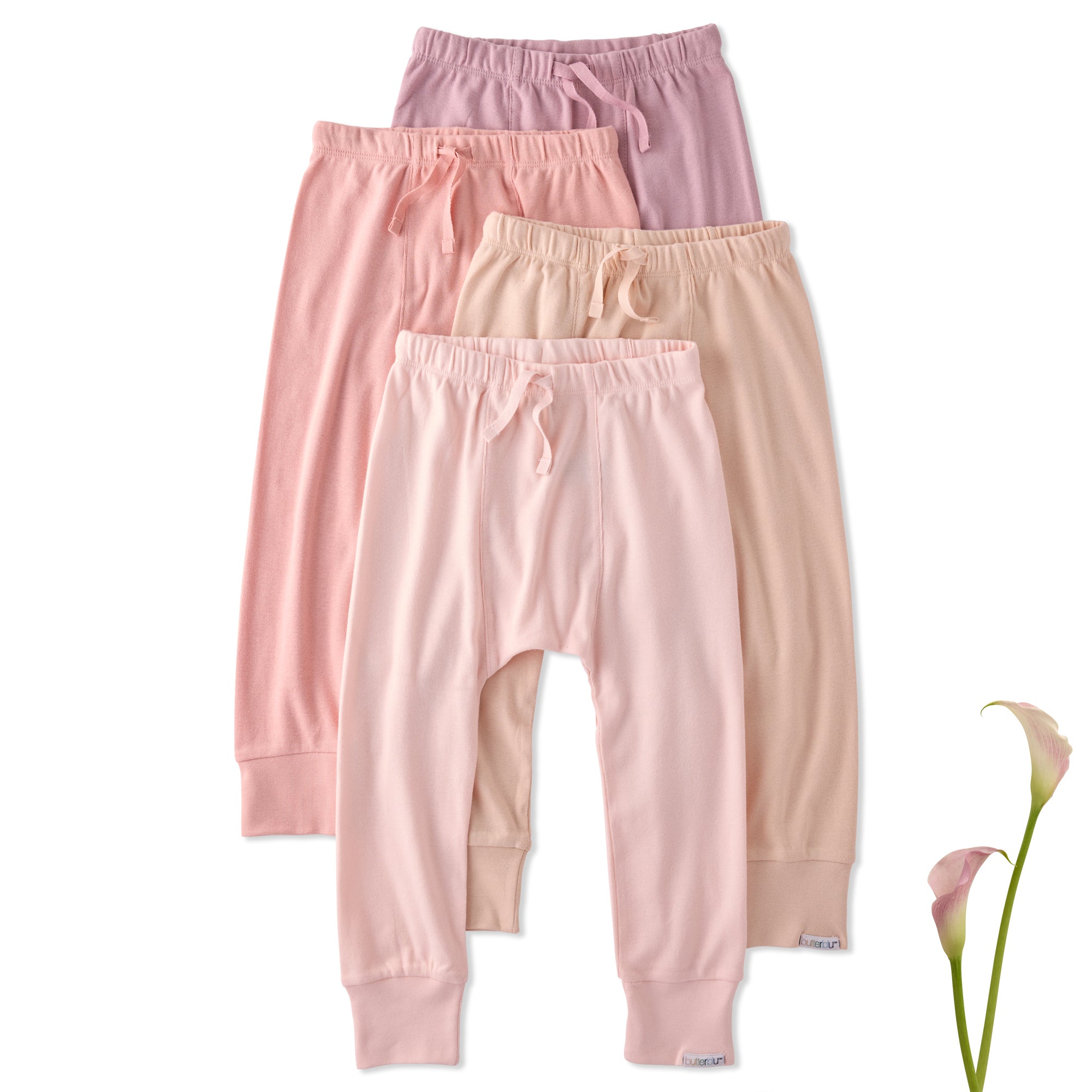 Three pairs of pink baby pants stacked on a white background with a flower.