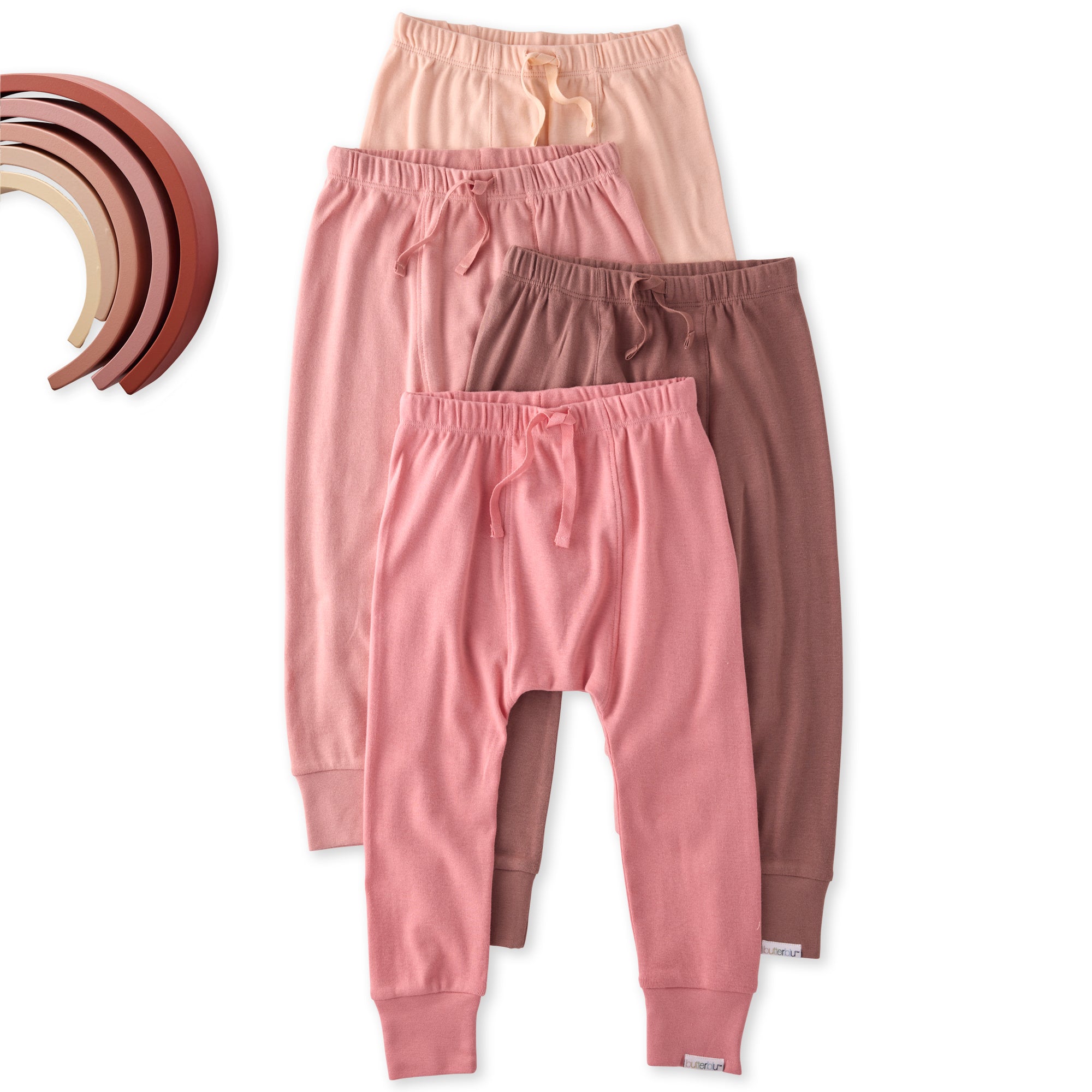 Three pairs of pink and brown kid pants on a white background with wooden rings.