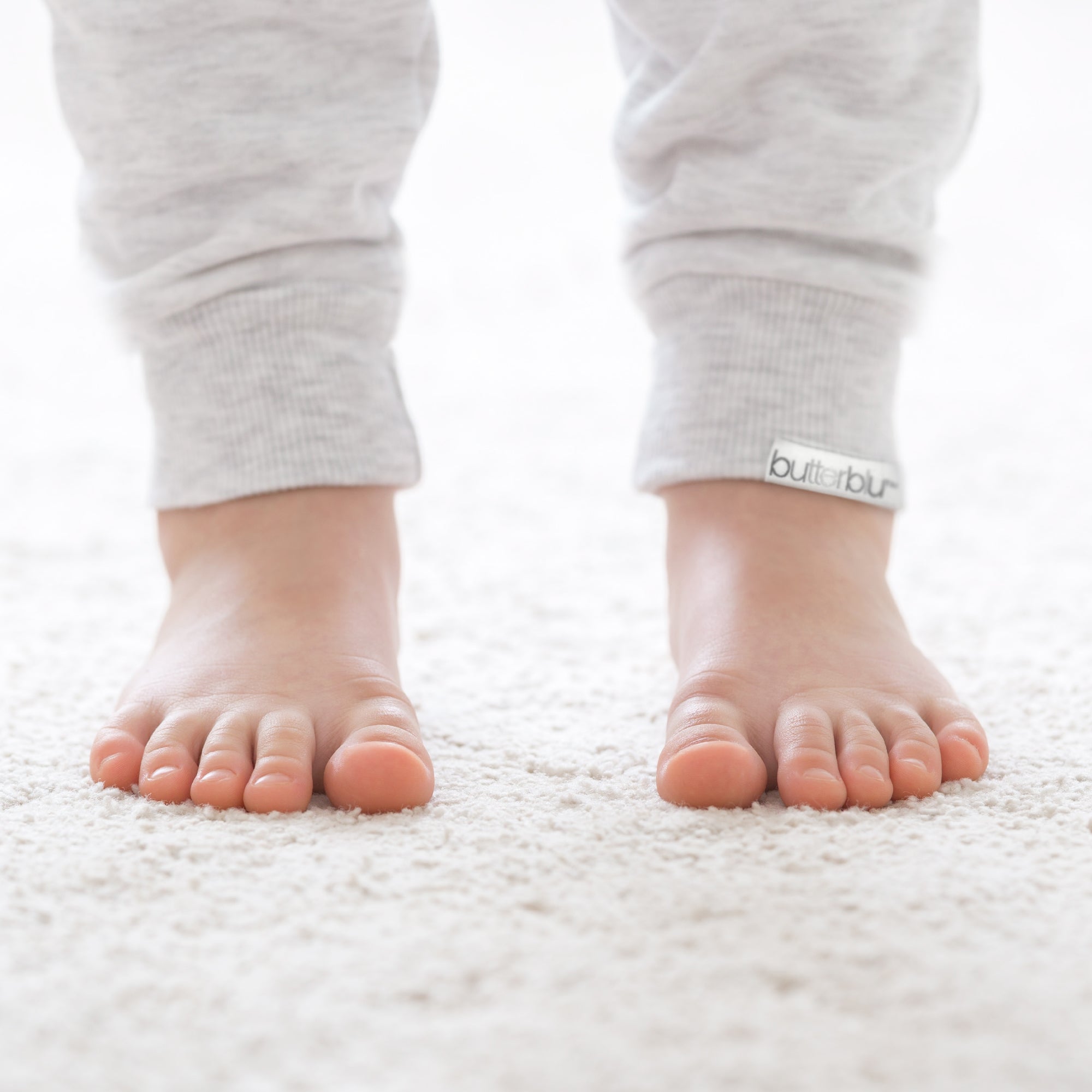 Baby's feet wearing gray pants with a visible brand logo on a white background