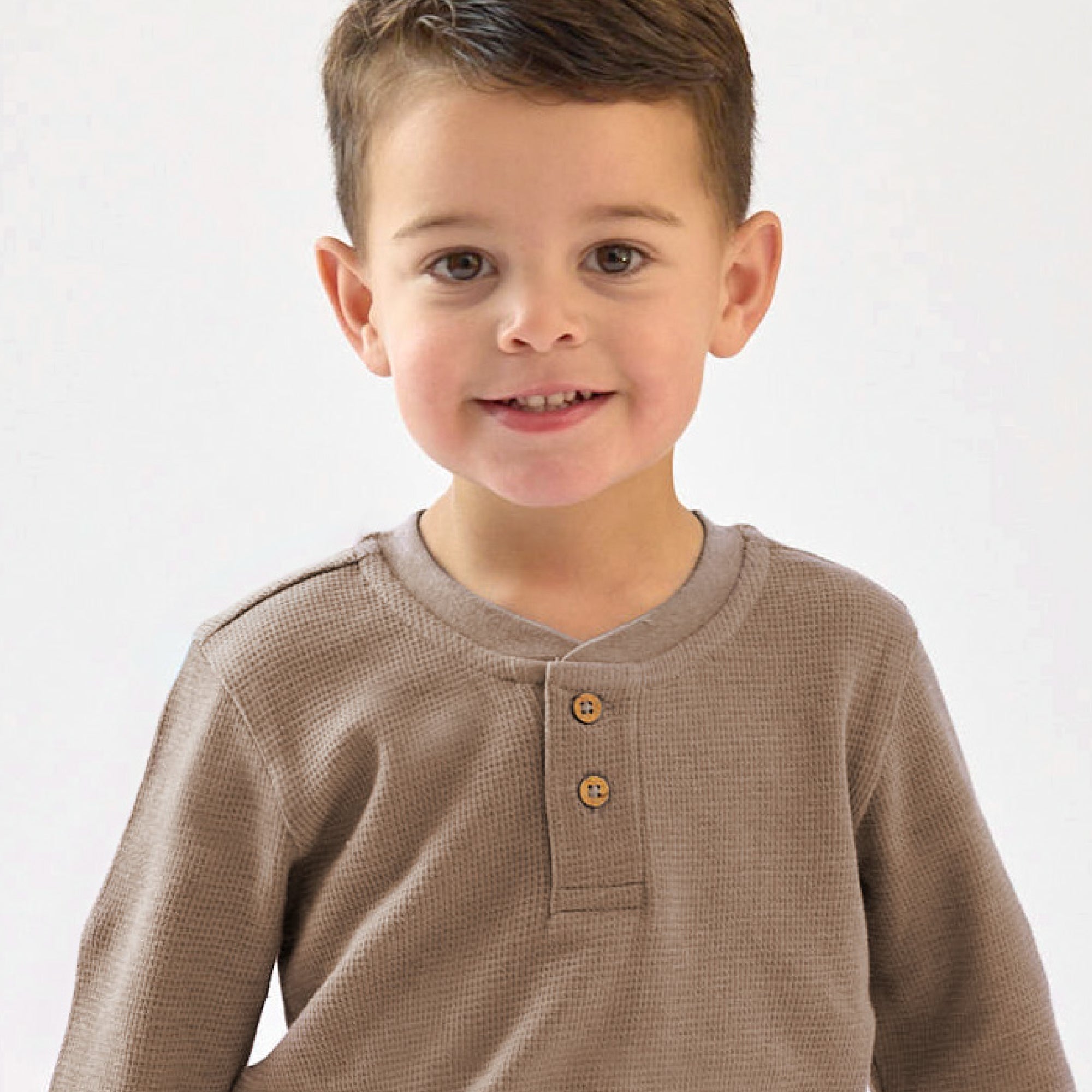Young boy wearing a brown long-sleeve shirt with buttons on a white background