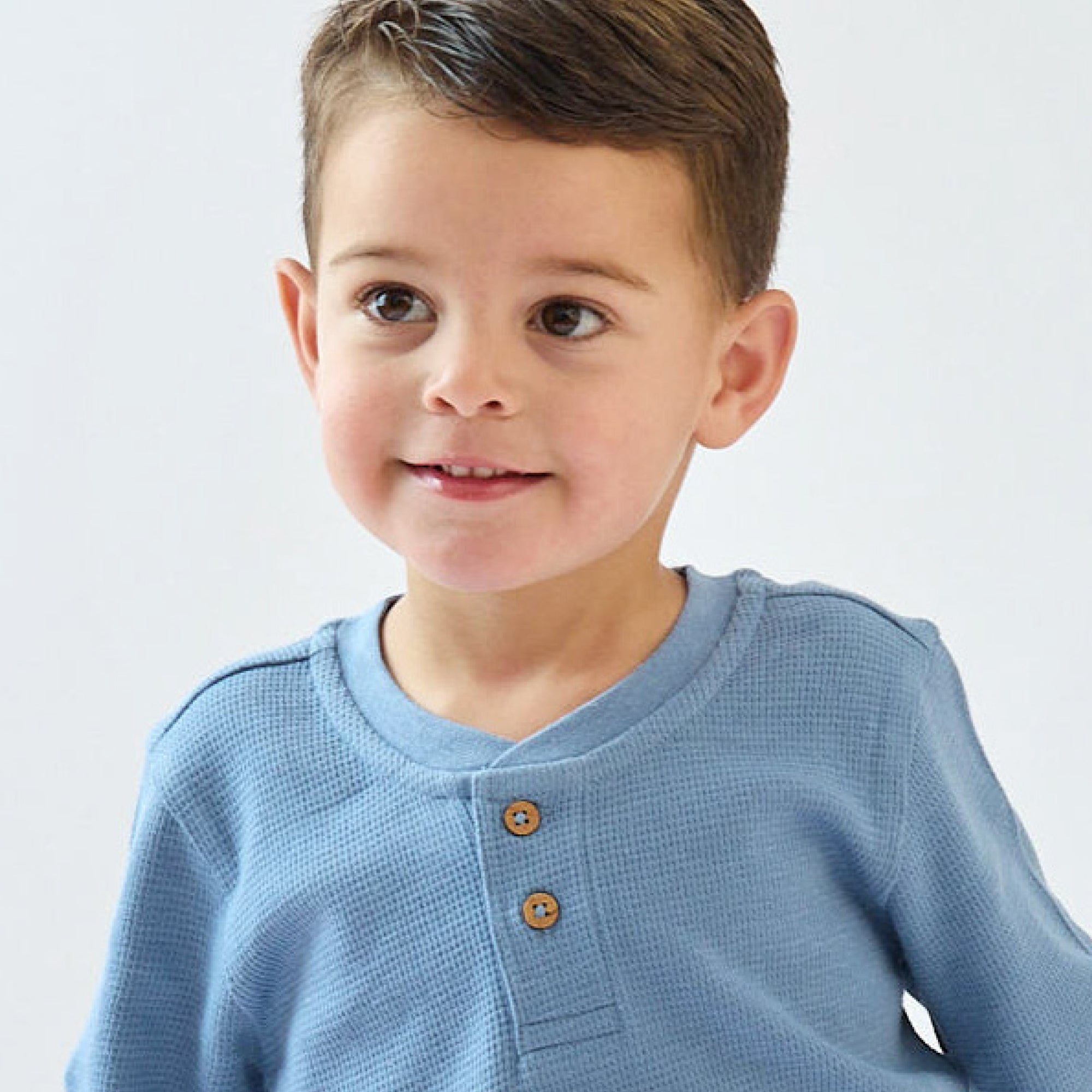 Child wearing a light blue shirt with brown buttons on a white background