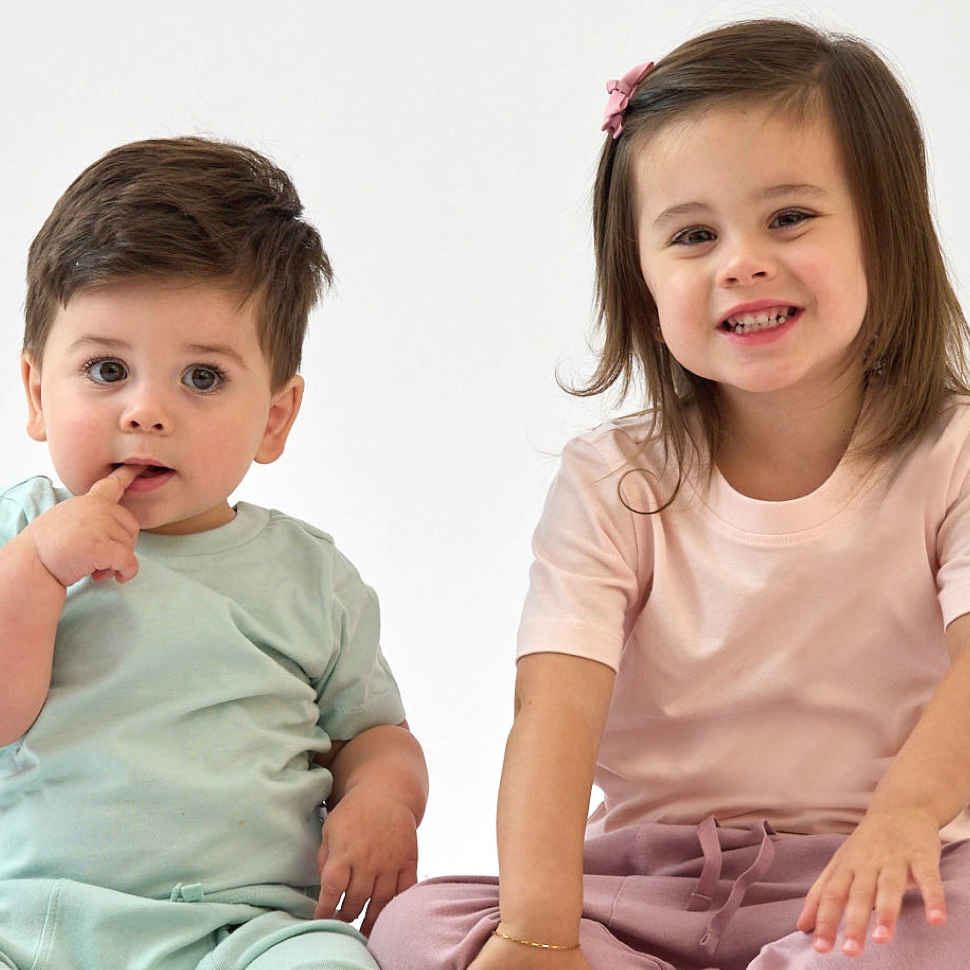 Two children, a boy and a girl, sitting side by side on a white background.