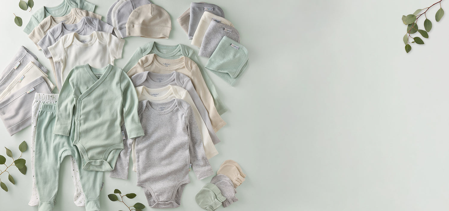 Collection of baby clothes including onesies, rompers, and hats on a light background.